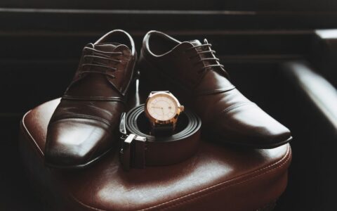Close-up of stylish men's shoes, belt, and wristwatch on a leather chair, showcasing elegance and fashion.