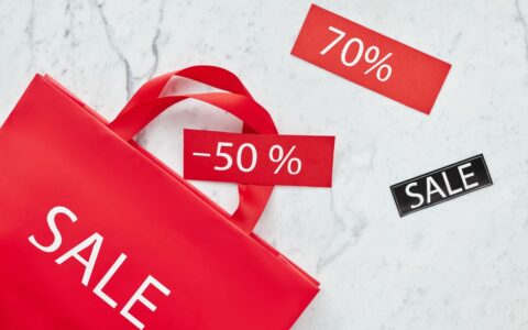 Red sale bag with 50% and 70% discount tags on marble background, perfect for retail promotions.