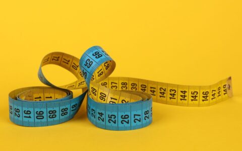 A coiled blue and yellow measuring tape on a bright yellow background.