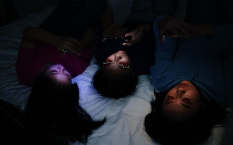 Three young women browsing their smartphones in a dimly lit room, sharing a moment of leisure.