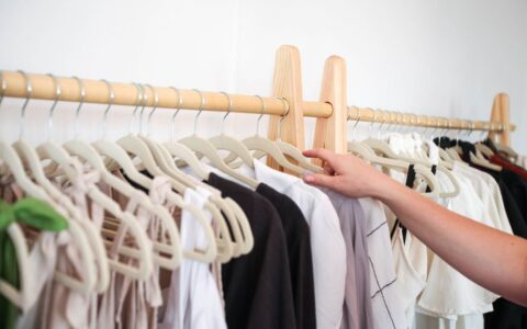 A person choosing clothing from a neatly arranged wardrobe rack indoors.