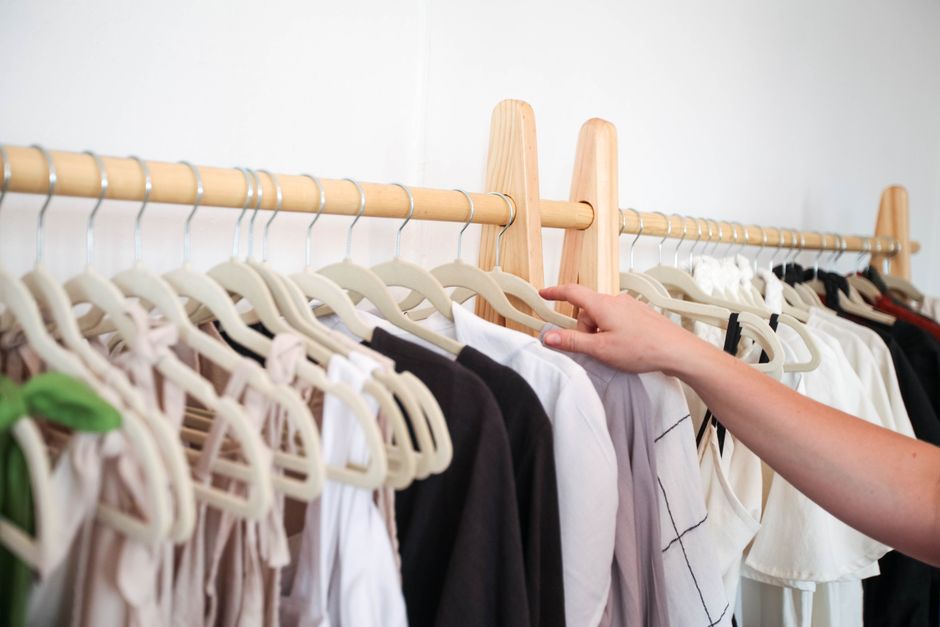 A person choosing clothing from a neatly arranged wardrobe rack indoors.