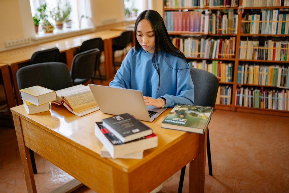 A teenager intensely focused on studying with a laptop in a library setting.