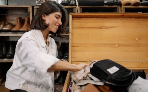 A young woman smiles as she sorts through clothes in a vintage store's wooden box.